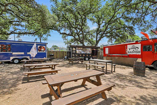 A picnic area with a blue and red food truck and wooden tables. at Park South Apartments, Austin, TX, 78748
