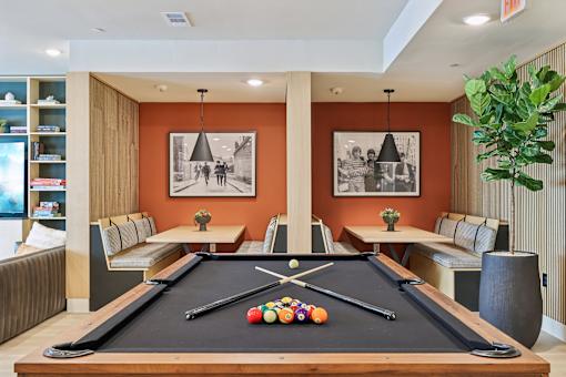 A pool table in a room with orange walls and two framed pictures hanging above it.