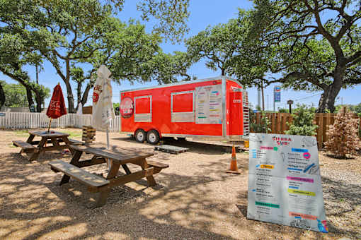 A red food truck is parked next to a picnic table with a sign in front of it. at Park South Apartments, Austin, 78748