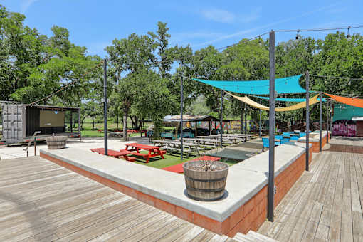 A wooden deck with a barrel and picnic tables. at Park South Apartments, Austin