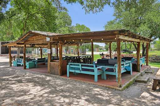 A wooden pavilion with blue benches is surrounded by trees. at Park South Apartments, Austin, Texas