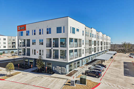 A modern apartment building with a red and white sign that says at ThreeTwenty at the Vybe Apartments, Kyle, 78640