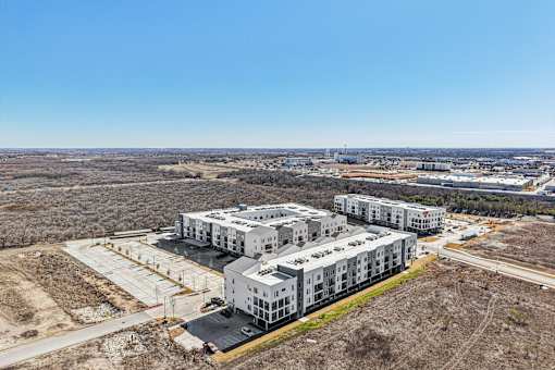 A large white building complex with a parking lot in front. at ThreeTwenty at the Vybe Apartments, Kyle, 78640