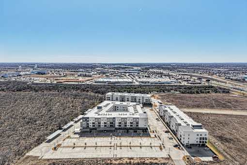 A large white building complex with a parking lot in front. at ThreeTwenty at the Vybe Apartments, Kyle, TX