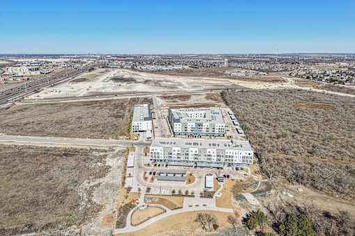An aerial view of a large building complex surrounded by a barren landscape. at ThreeTwenty at the Vybe Apartments, Kyle, Texas