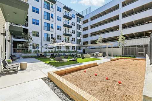 A sandbox with red balls in the middle of a concrete area surrounded by buildings.