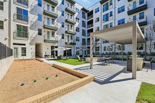 A modern apartment complex with a sandy courtyard and a wooden pergola.