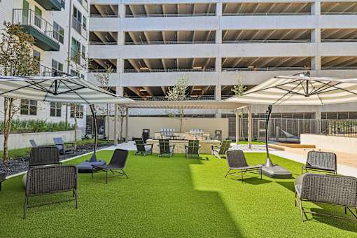 A patio area with chairs and tables is surrounded by a parking garage.