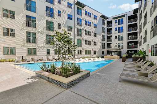 A pool surrounded by buildings and lounge chairs.