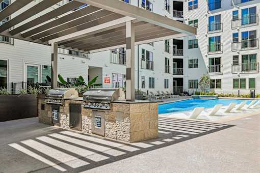A pool area with a grill and a building in the background.