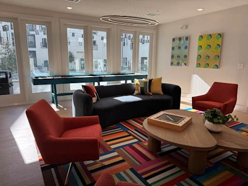 A living room with a black couch, a red chair, a wooden coffee table, and a colorful rug. at ThreeTwenty at the Vybe Apartments, Kyle, 78640