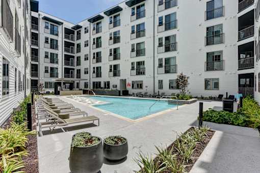 A pool surrounded by lounge chairs and planters in front of apartment buildings.