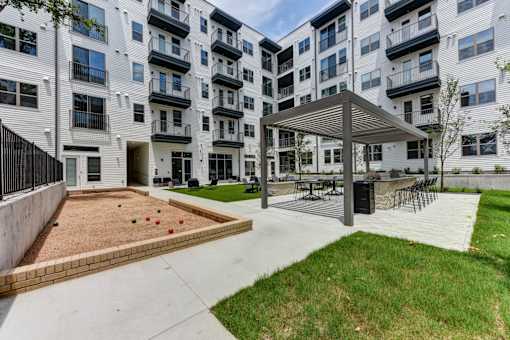 A playground area with a sandbox and a pavilion is located in front of a white apartment building.