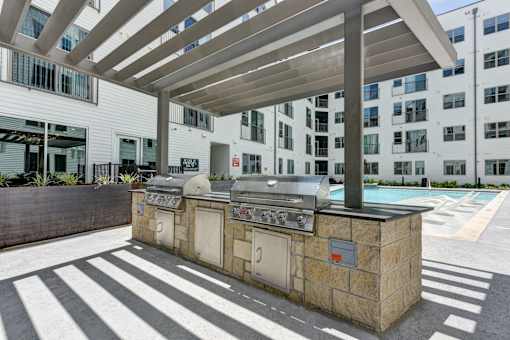 A bbq grill is under a wooden canopy on a patio.