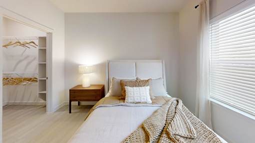 A bedroom with a bed, nightstand, and window with blinds.