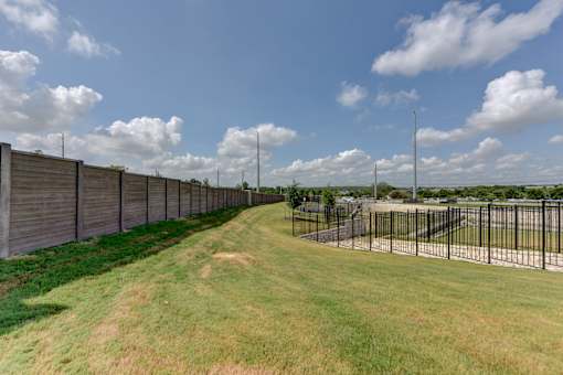 Fenced perimeter with green space and pathways at Cantarra Apartments, Manor, Texas