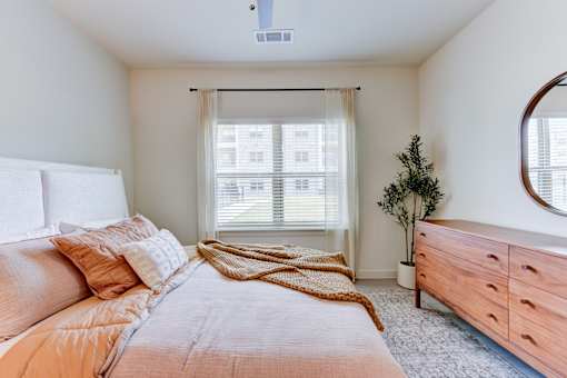 Cozy bedroom with wood dresser and plants at Cantarra Apartments, Manor