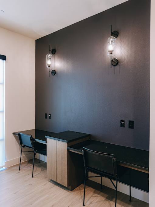 A black desk with two chairs and two wall lamps.