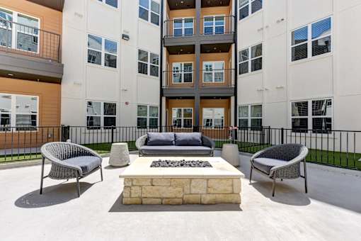 A modern outdoor seating area with a stone fireplace in front of a multi-story apartment building.