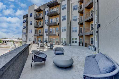 A modern apartment complex with a rooftop patio furnished with a couch, chairs, and ottoman.