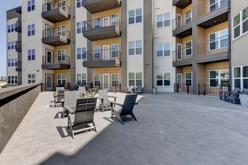 A large outdoor patio area with chairs and tables in front of apartment buildings.