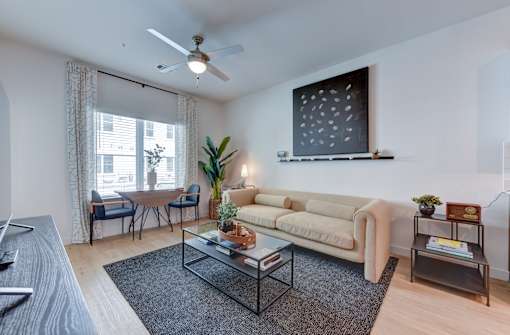 A living room with a beige couch, a glass coffee table, and a ceiling fan.