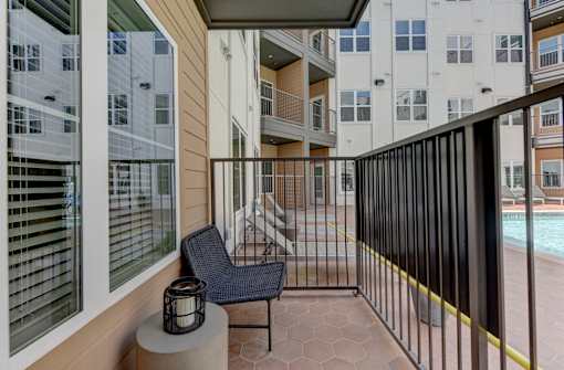 A balcony with a black chair and a lantern on a table.