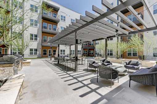 A patio with a black metal pergola and grey wicker chairs.