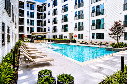 A pool surrounded by lounge chairs and potted plants.