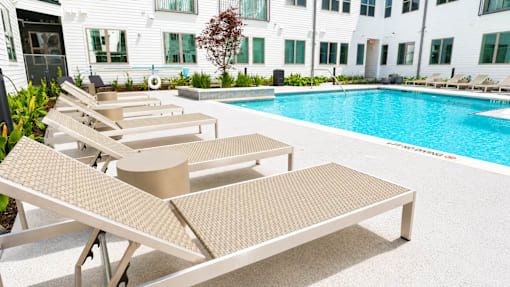 A pool with sun loungers in front of a white building.