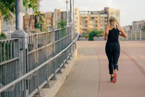 A woman is running on a sidewalk next to a metal fence.
