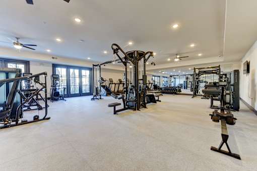 A spacious gym with a variety of equipment including treadmills, weights, and a ceiling fan.