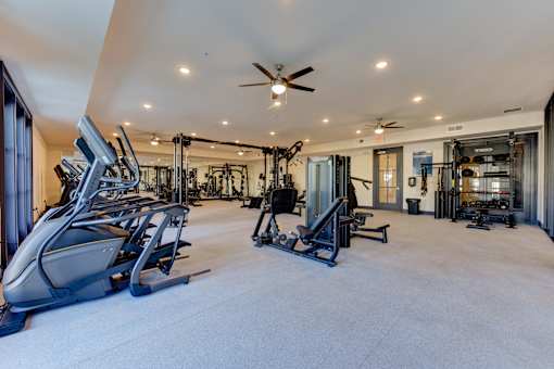A spacious gym with a variety of equipment and a ceiling fan.