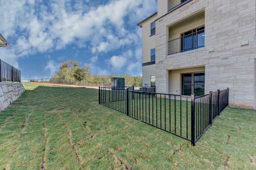 A black metal fence surrounds a grassy yard in front of a two-story building.