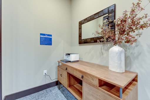 A wooden desk with a white vase and a mirror on the wall.