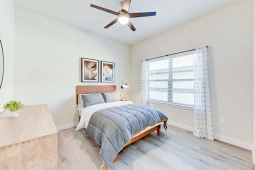 A bedroom with a bed, a ceiling fan, and a window with curtains.