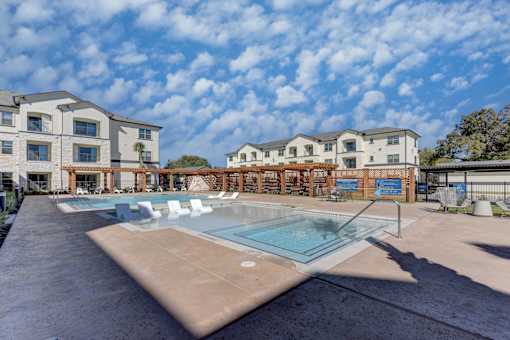 A swimming pool in front of a building with a blue sky and clouds in the background.
