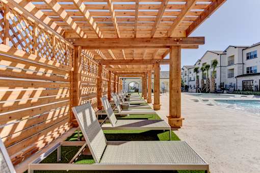 A wooden pergola with lounge chairs is situated on a sandy beach.