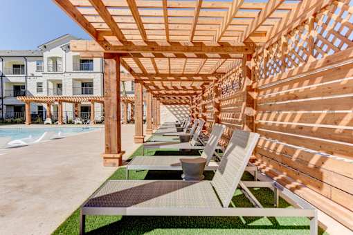 A wooden pergola with benches is in the foreground of a building.