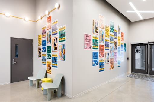 A hallway with a wall of posters and two chairs.