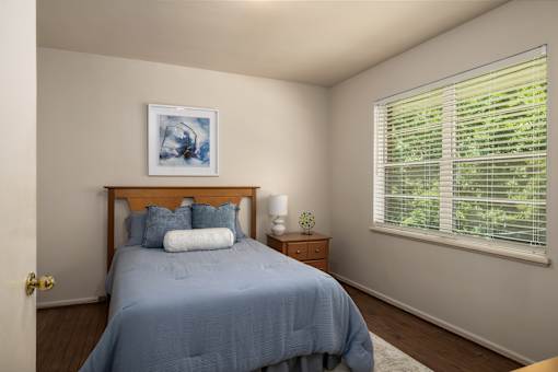 A bedroom with a bed, nightstand, and a window with blinds.