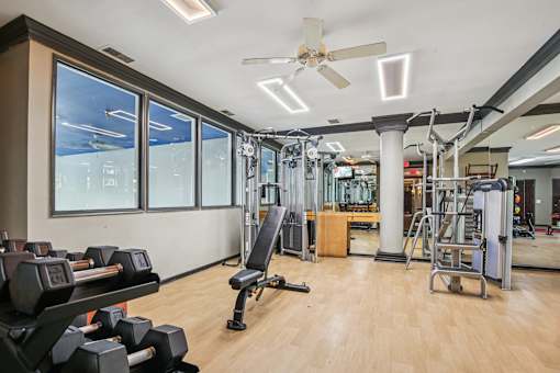A gym with a variety of equipment including dumbbells, weight plates, and a bench press.