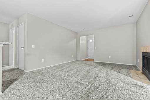 A large, empty room with a fireplace and carpeted floor.