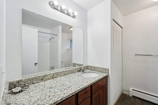 A bathroom with a granite countertop and a mirror above it.