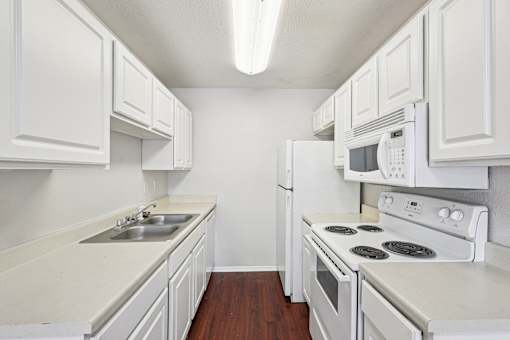 A white kitchen with a stove, oven, microwave, and sink.