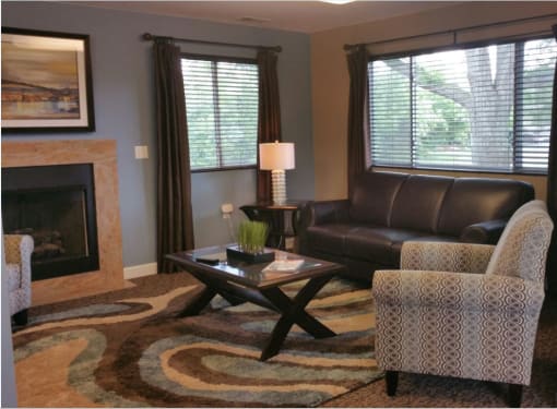 The leasing office at Brighton Cove. There is a leather couch under a big picture window. An end table with a lamp is to the left of the couch. A stripped chair is to the right of the couch. A glass and wooden coffee table is in front of the couch. Under it is a brown, tan, and blue pattered rug.