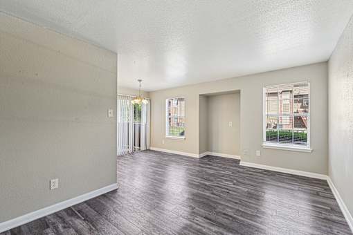 A spacious room with wood flooring and two windows.