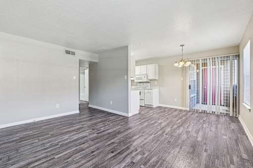 A room with wooden flooring and a kitchenette in the background.
