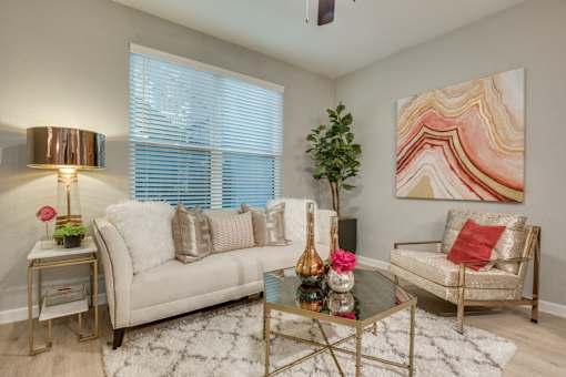 A living room with a white couch, a glass coffee table, and a painting on the wall.