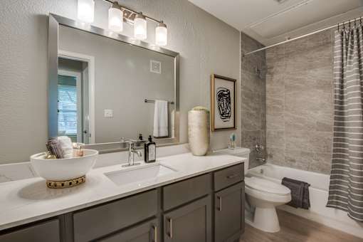 A bathroom with a white counter top and a large mirror above it.
